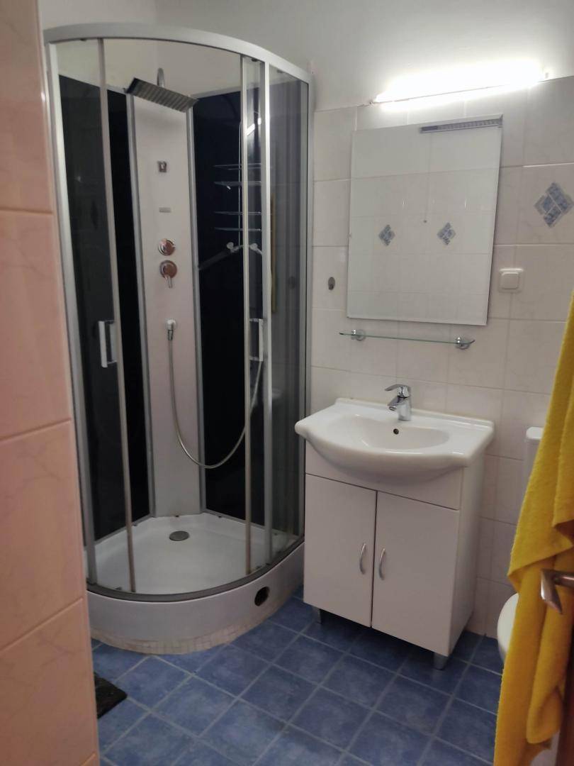 Badezimmer mit Eckduschkabine, Waschbeckenunterschrank und blauen Bodenfliesen.