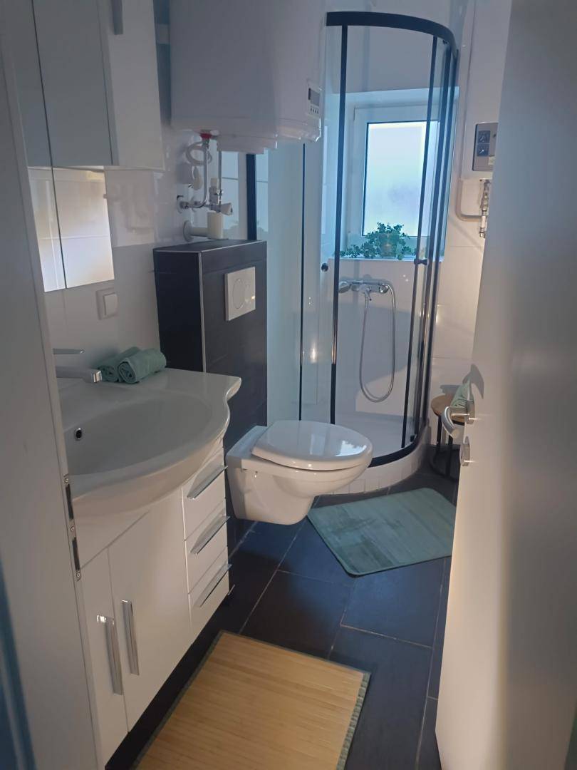 Modernes Badezimmer mit Duschkabine, WC, Waschbecken und Fenster für Tageslicht.