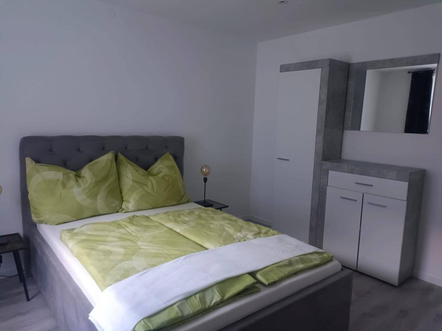 Schlafzimmer mit Doppelbett, Nachttisch und modernem Kleiderschrank mit Spiegel.