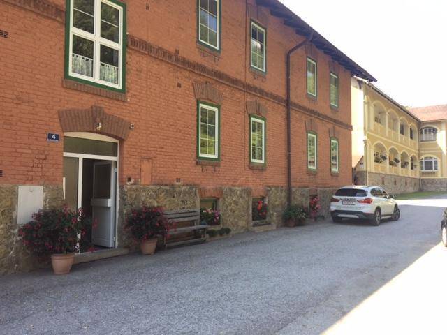 Backsteingebäude mit weißen Fenstern und grünen Rahmen sowie einem geparkten Auto davor.