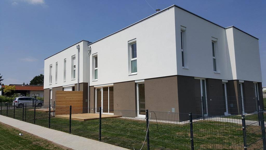 Modernes Neubaugebäude mit weißer und grauer Fassade, großen Fenstern und einer kleinen Holzterrasse.