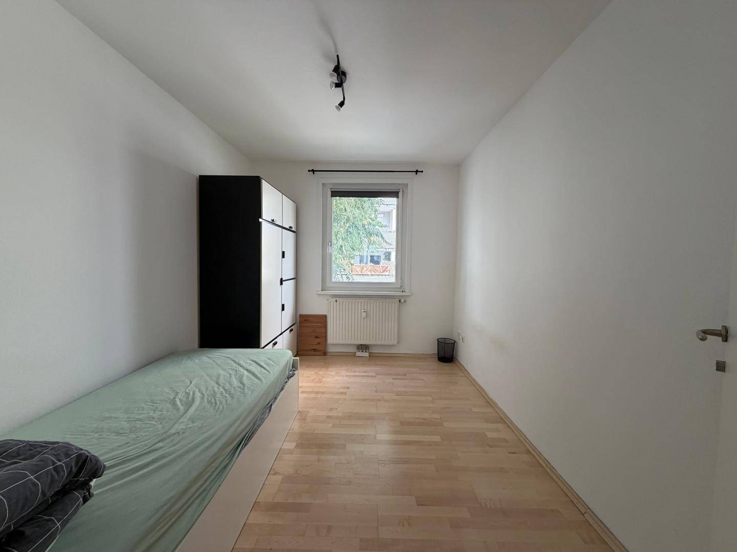 Einfaches Schlafzimmer mit Einzelbett, Kleiderschrank und Holzboden.