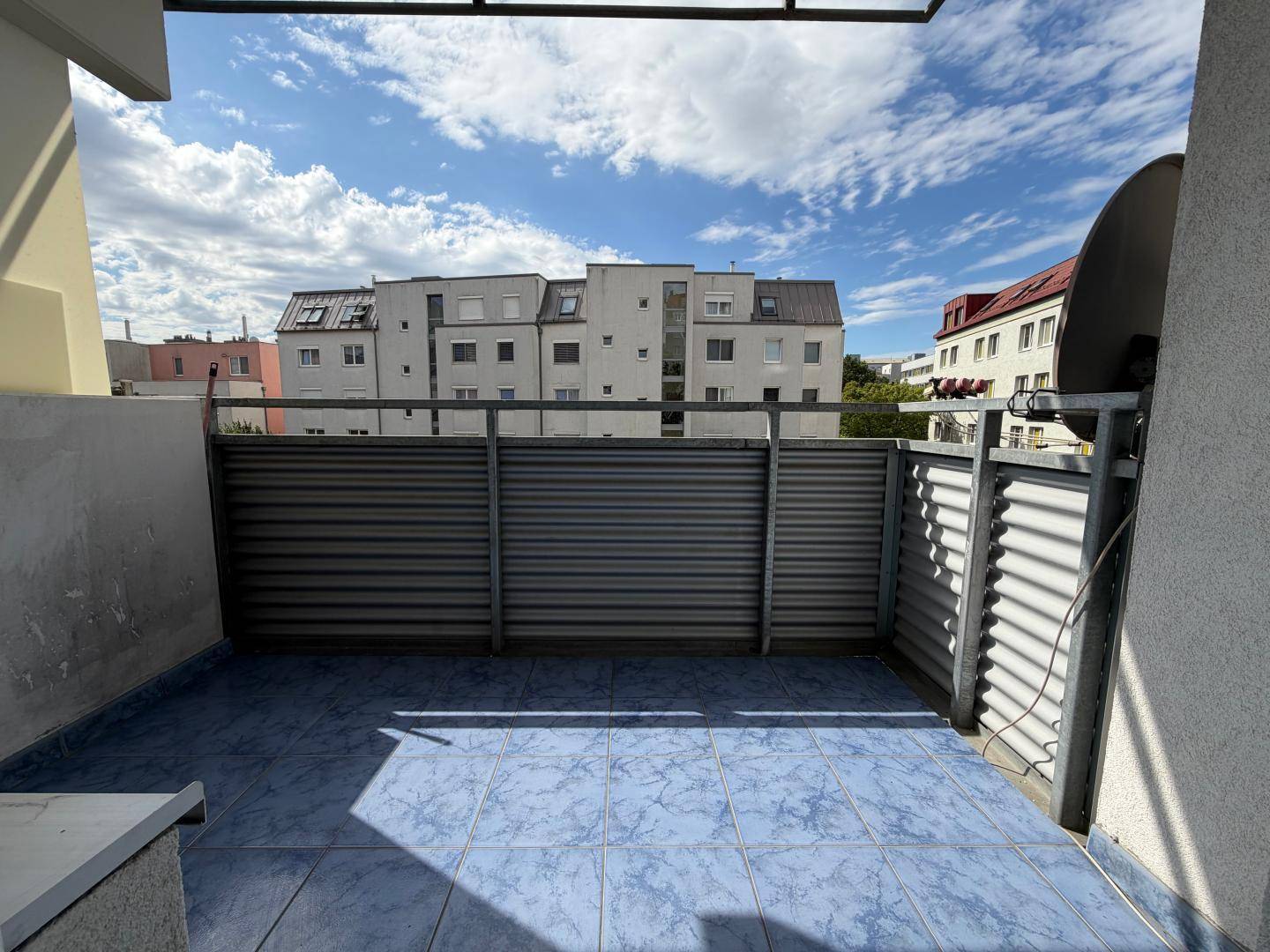 Kleiner Balkon mit blauen Fliesen und Blick auf umliegende Gebäude.