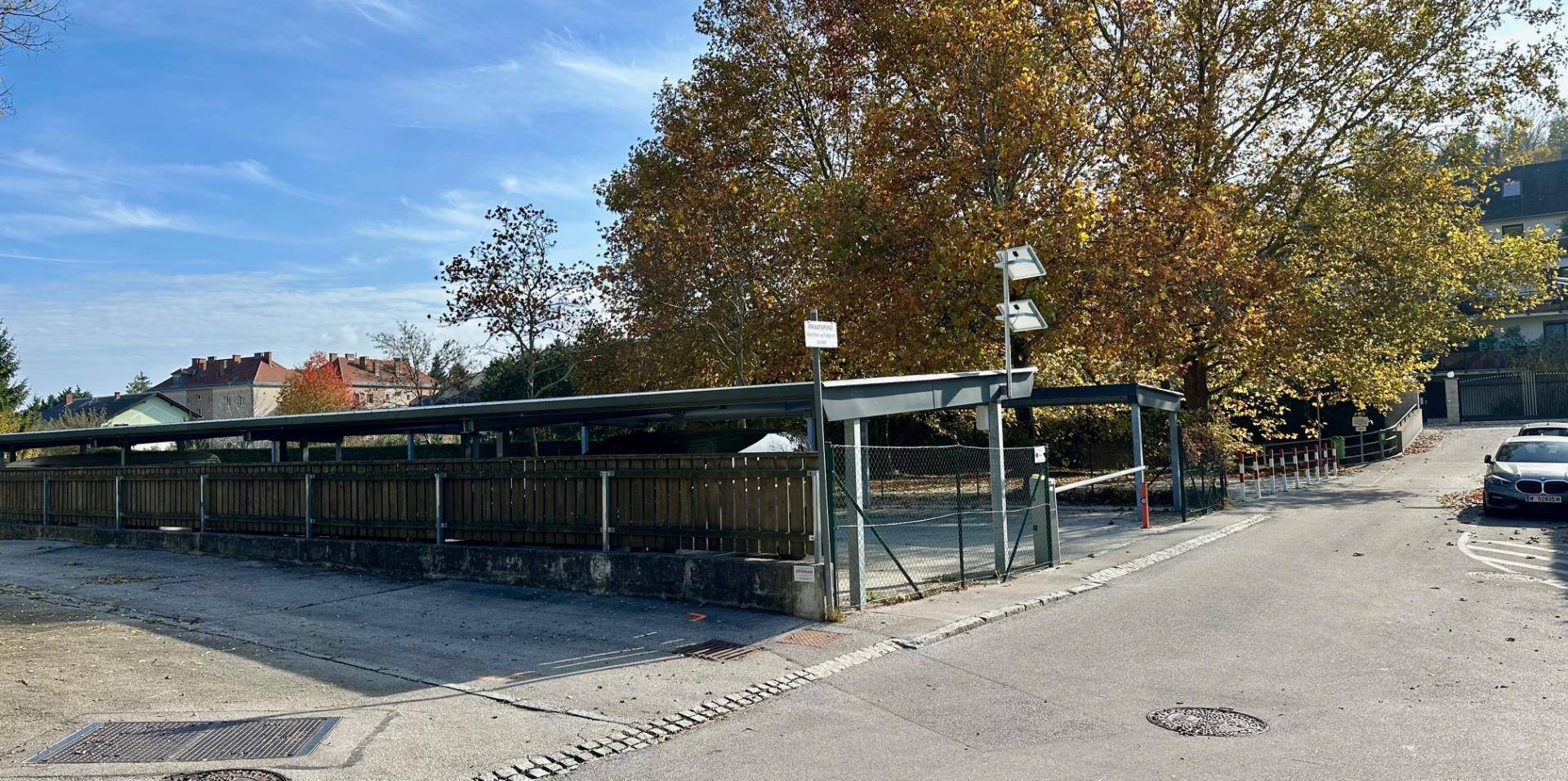 Weitläufige überdachte Parkflächen mit Herbstbäumen und Zufahrt zur Straße.