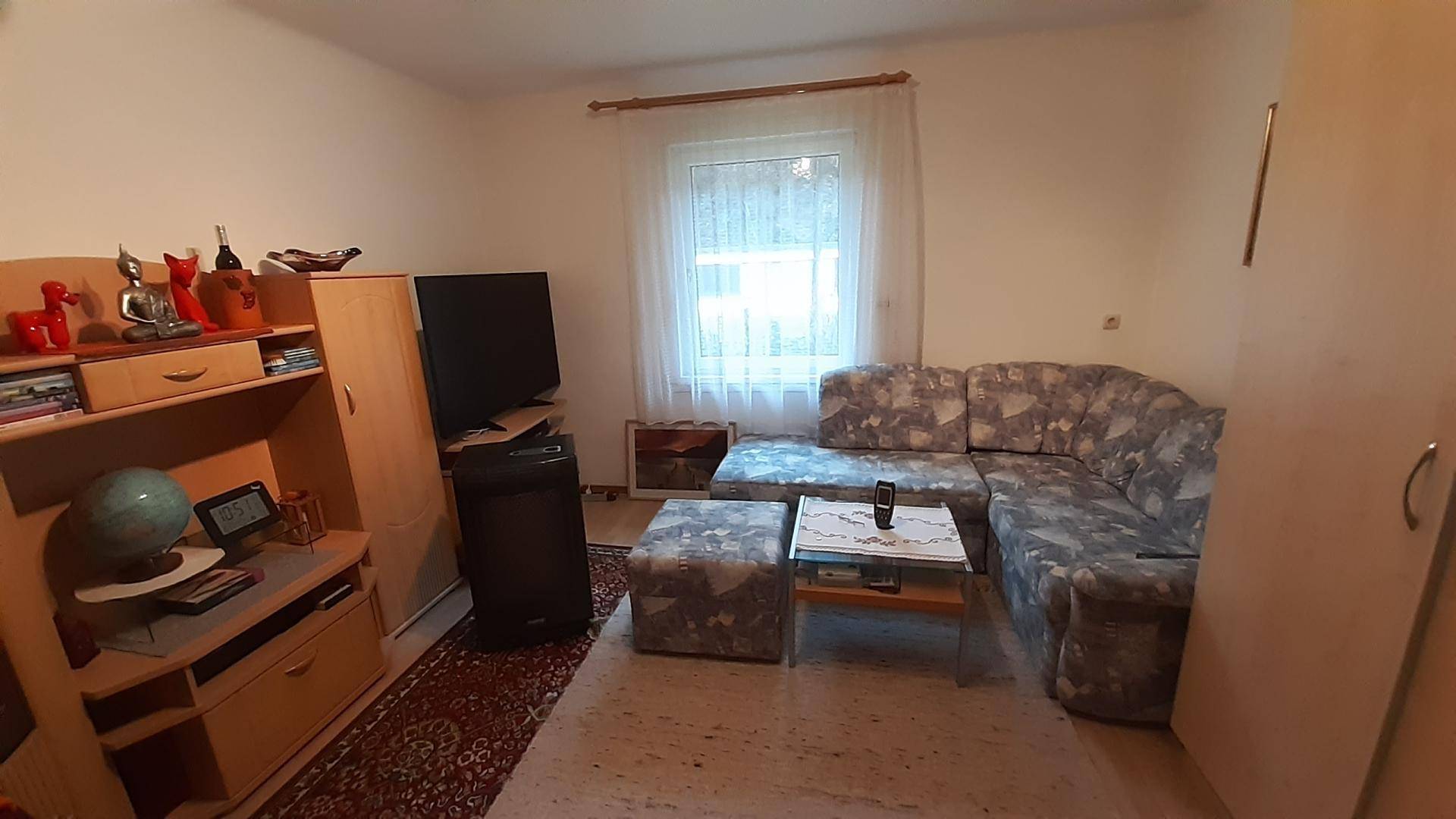 Wohnzimmer mit Ecksofa, Couchtisch, Teppich und einem Fenster, das Tageslicht hereinlässt.