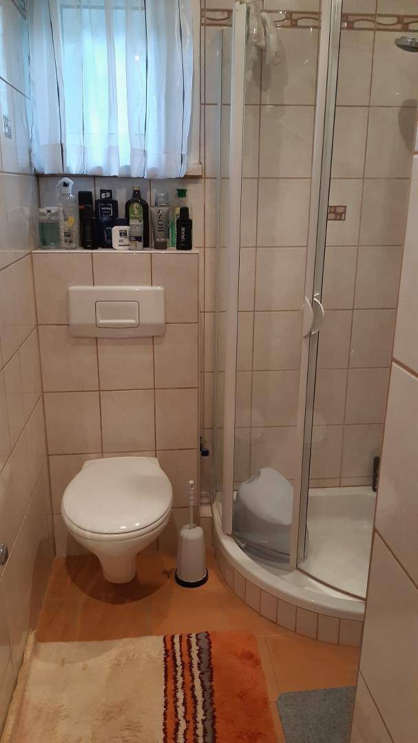 Badezimmer mit Duschkabine, wandhängendem WC, Fliesen und einem Fenster für natürliches Licht.