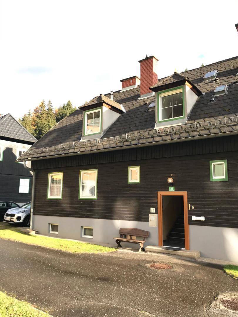 Traditionelles Haus mit dunkler Holzfassade, Satteldach, Dachgauben und einem Eingangsbereich mit Treppe.