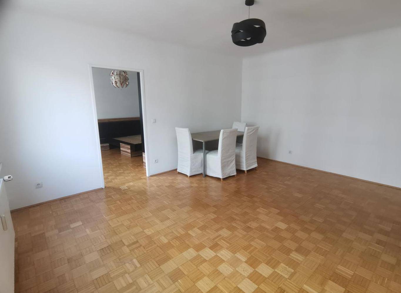 Geräumiger Wohn- und Essbereich mit Parkettboden und Zugang zu einem weiteren Zimmer.
