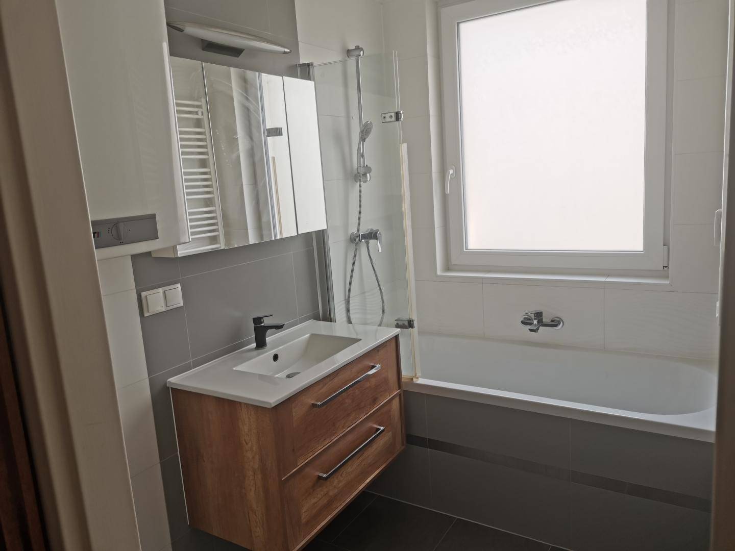Modernes Badezimmer mit Einzelwaschbecken, Badewanne, Duschfunktion und Spiegelschrank.