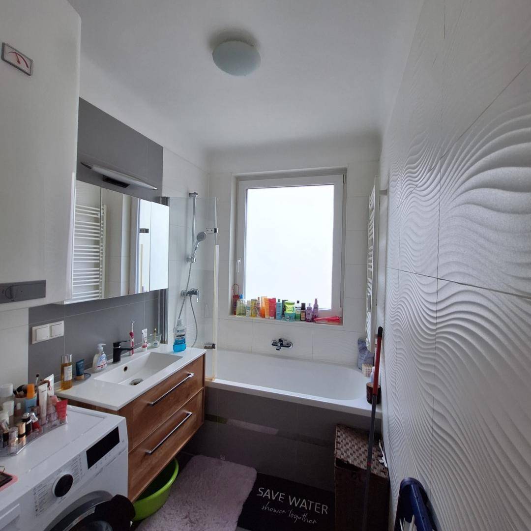 Helles Badezimmer mit Badewanne, Duschfunktion, Einzelwaschbecken und Fenster.