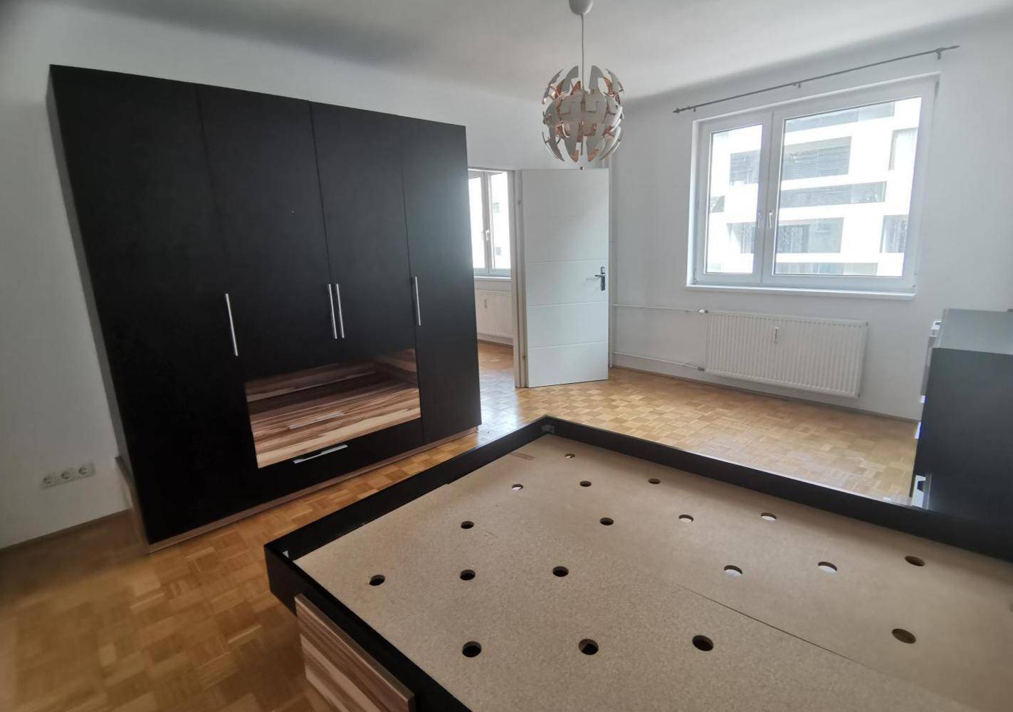 Schlafzimmer mit Parkettboden, großem Kleiderschrank und weitem Blick auf die Stadt.