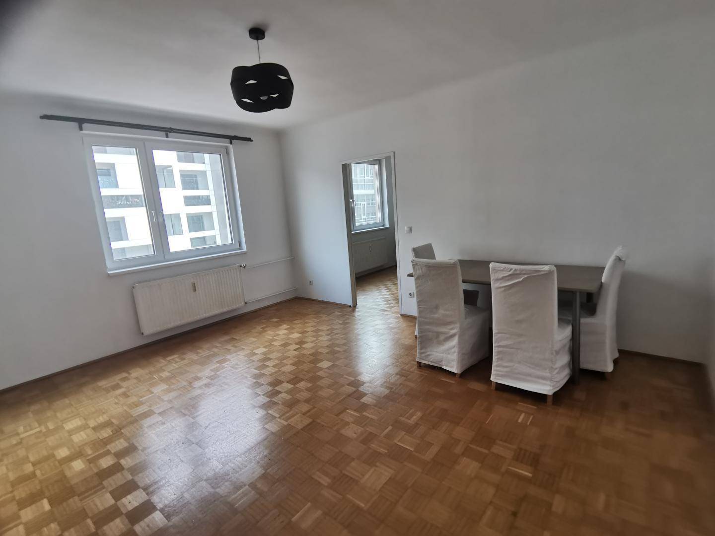 Heller Wohn- und Essbereich mit Parkettboden, großem Fenster und Esstisch.