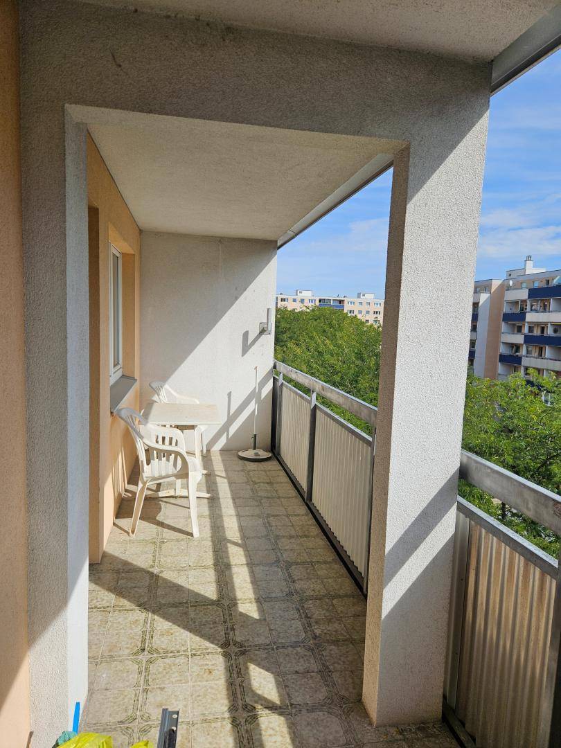 Sonniger Balkon mit Fliesenboden, Gartenmöbeln und einem angenehmen Blick ins Grüne.