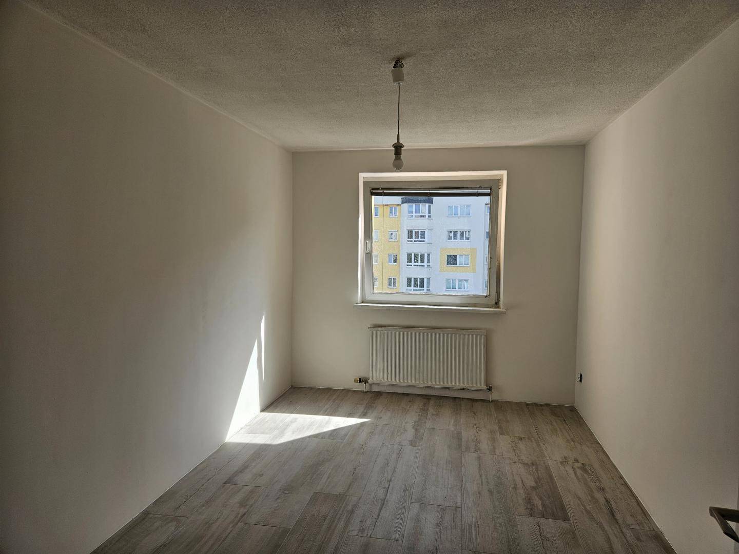 Helles Schlafzimmer mit Fliesenboden in Holzoptik und einem Fenster, das viel Sonnenlicht hereinlässt.