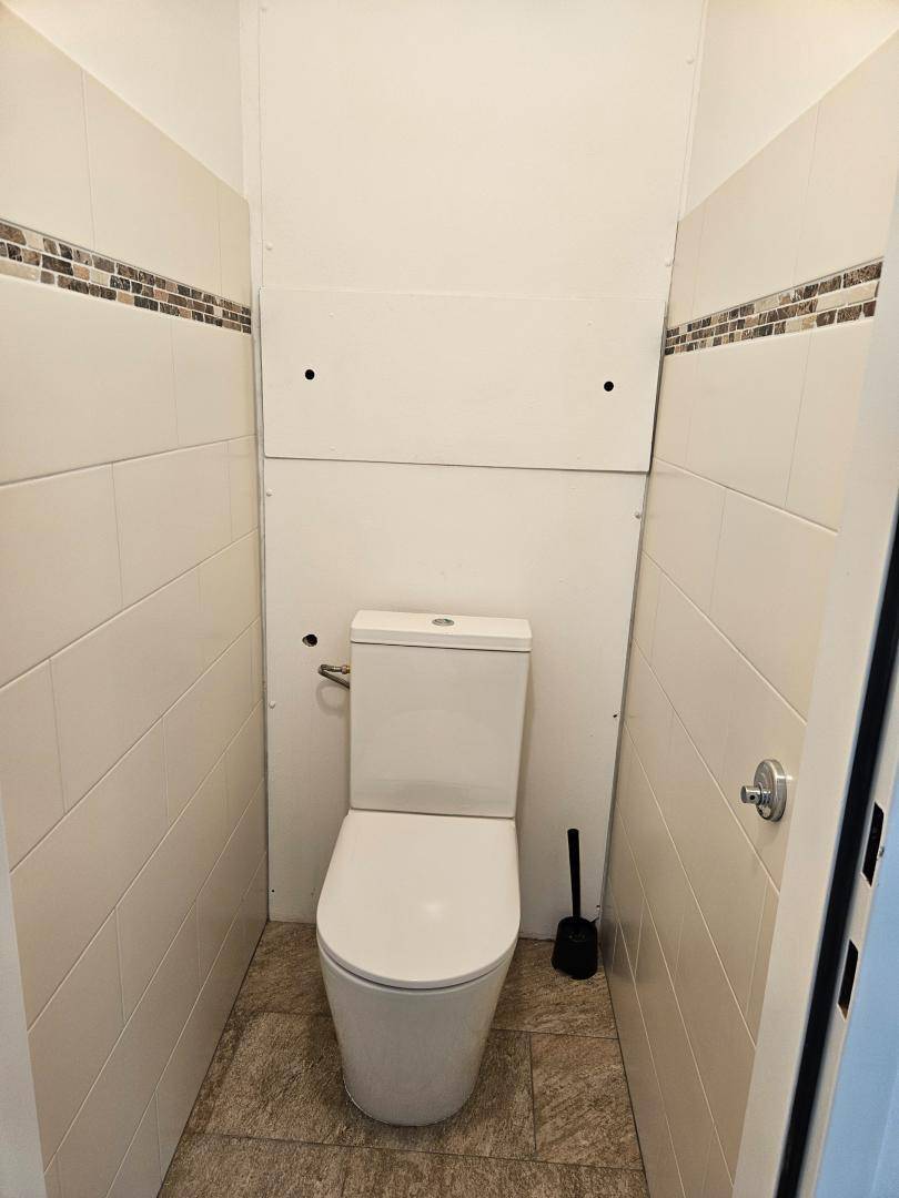 Sauberer Toilettenraum mit weißer Keramik, hellen Fliesen und einer dekorativen Bordüre.