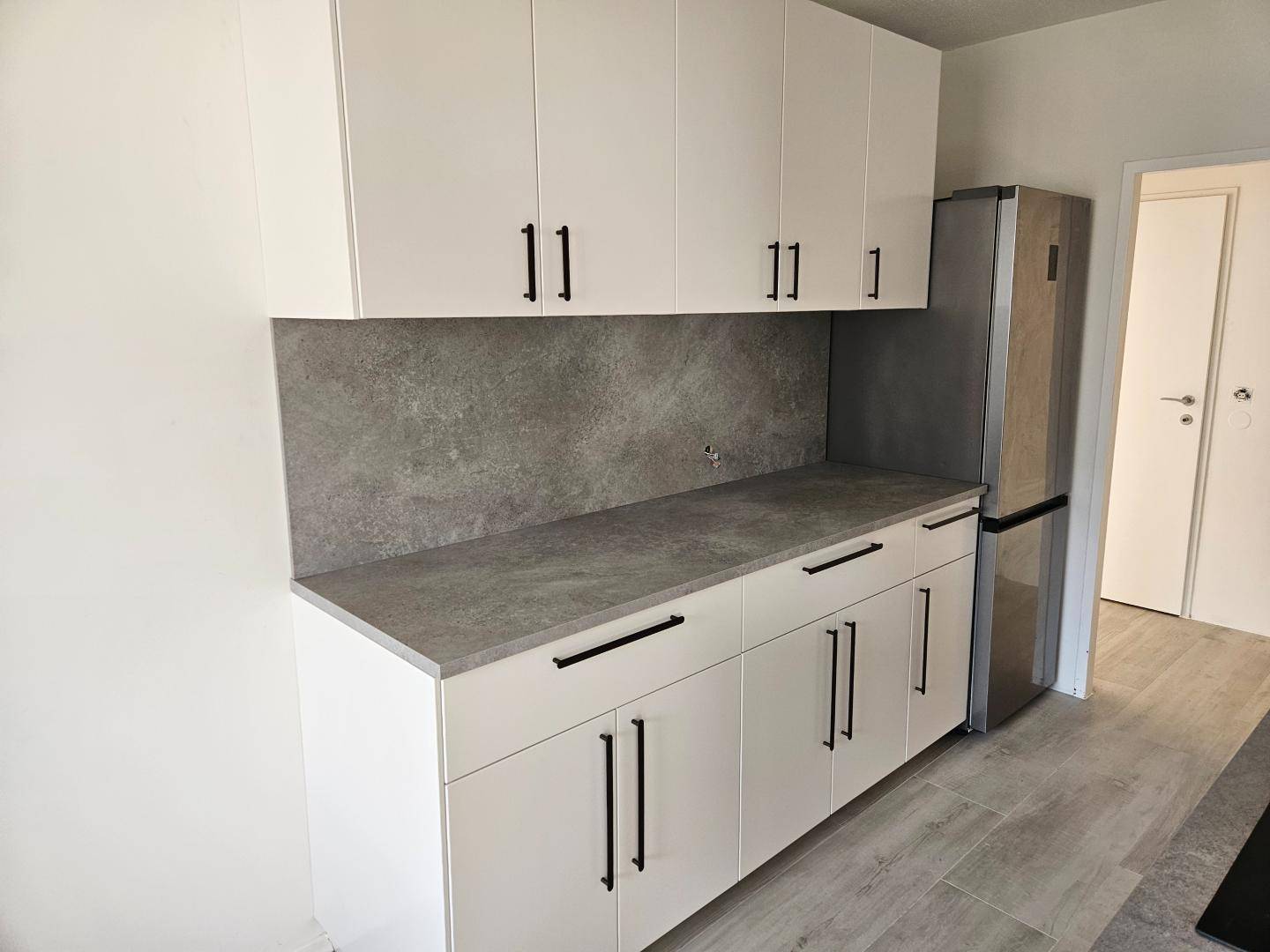 Moderne Küchenzeile mit weißen Hochglanzschränken, grauer Arbeitsplatte und integriertem Kühlschrank.