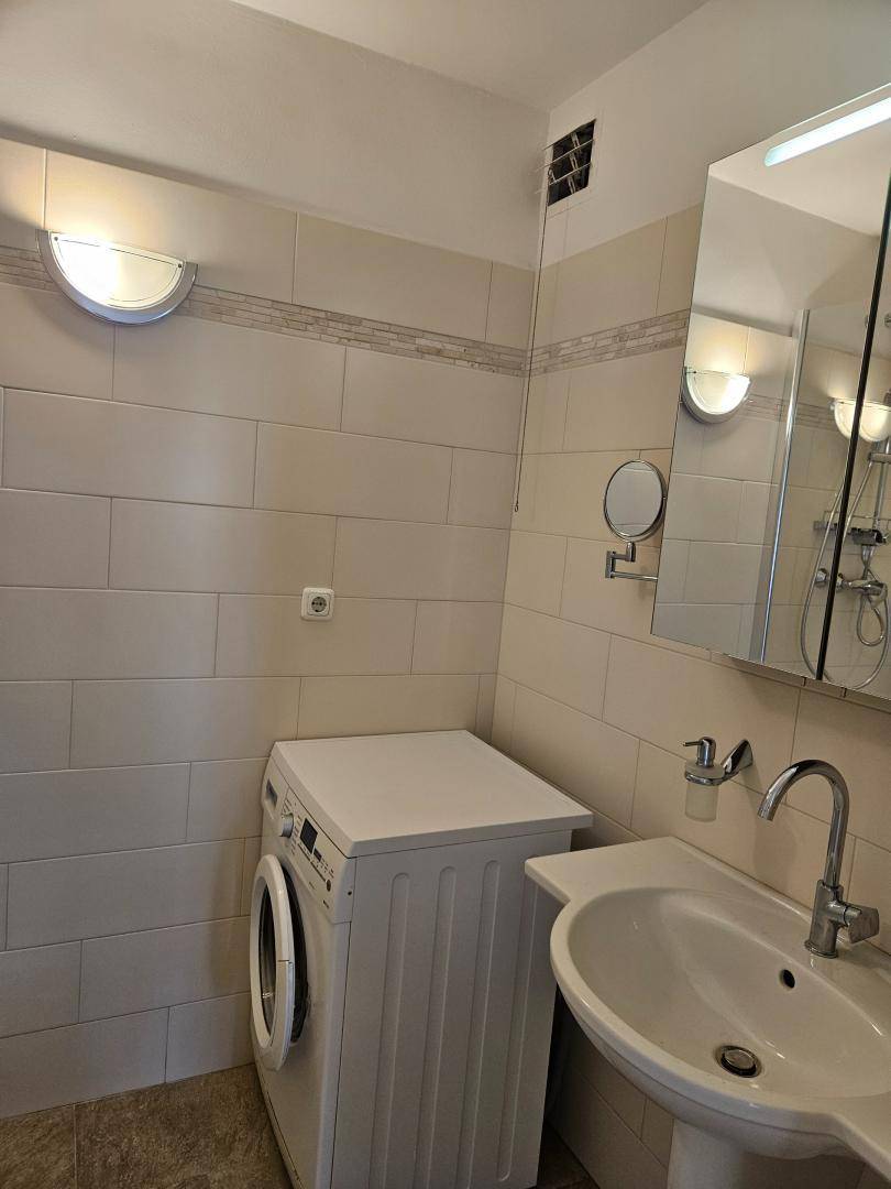 Helles Badezimmer mit Waschbecken, Spiegelschrank und einer Waschmaschine.