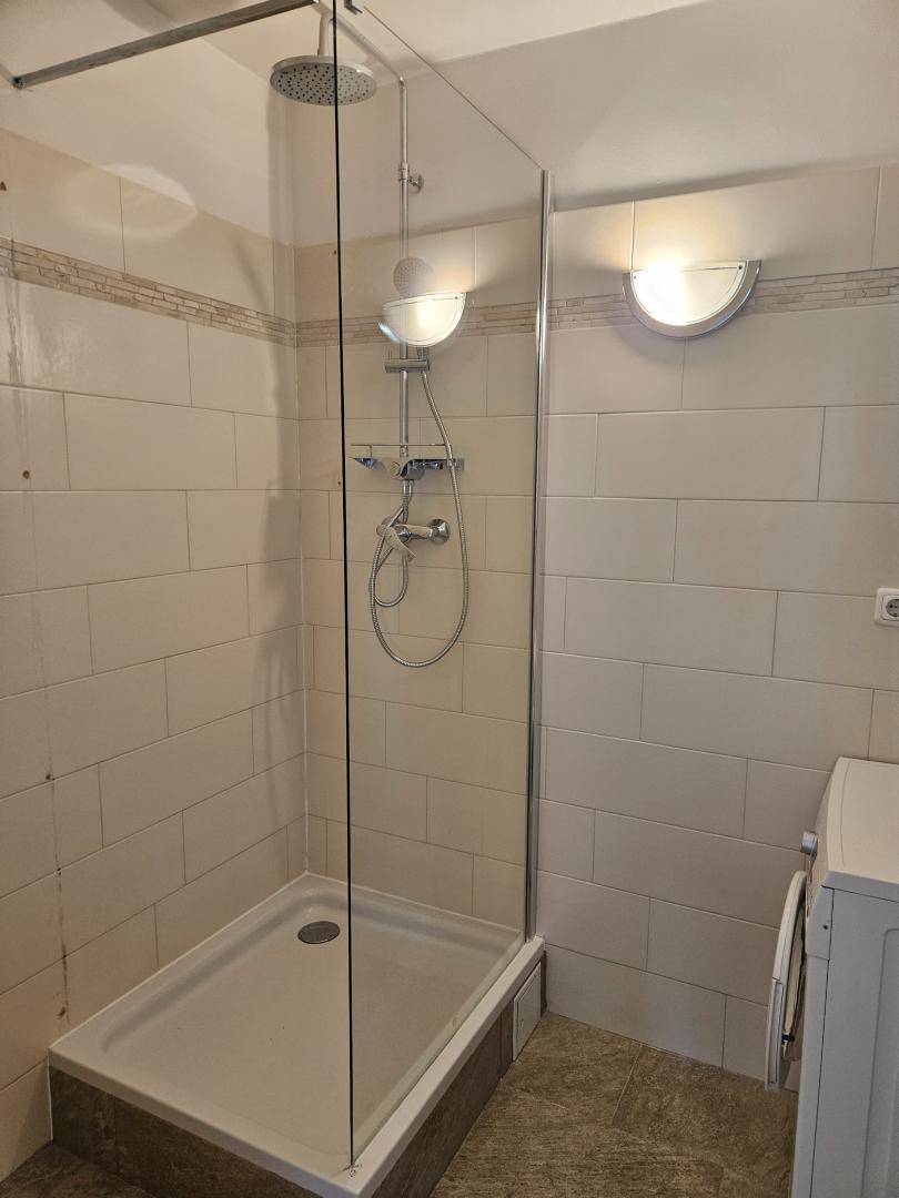Badezimmer mit moderner Glasdusche, Regenduschkopf und Anschluss für eine Waschmaschine.