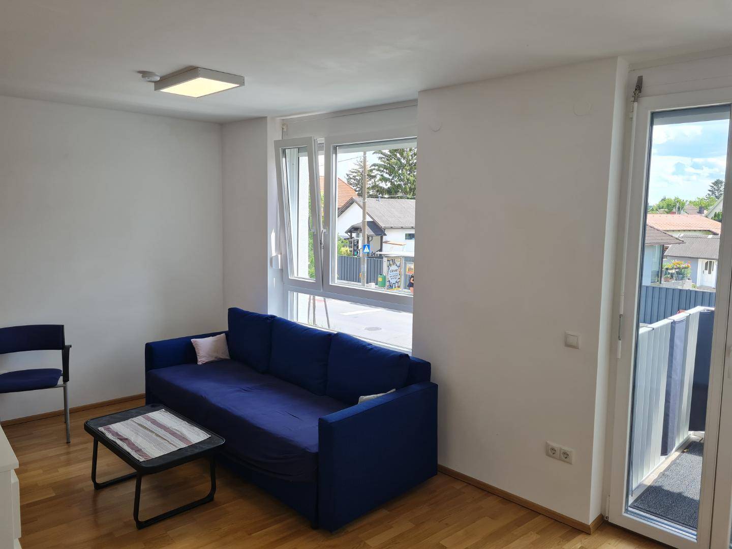 Helles Wohnzimmer mit blauem Sofa, großem Fenster und Zugang zum Balkon.