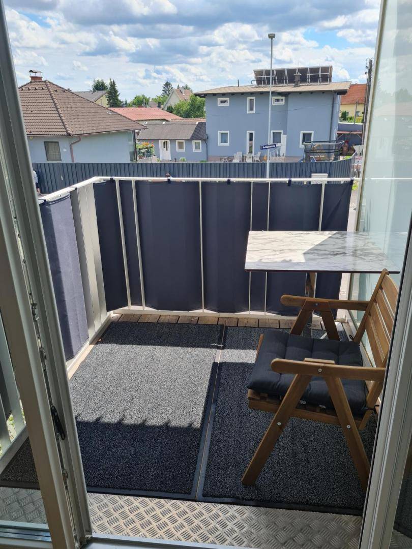 Kleiner Balkon mit Holzboden und Sitzgelegenheiten, bietet Blick auf die Nachbarschaft.