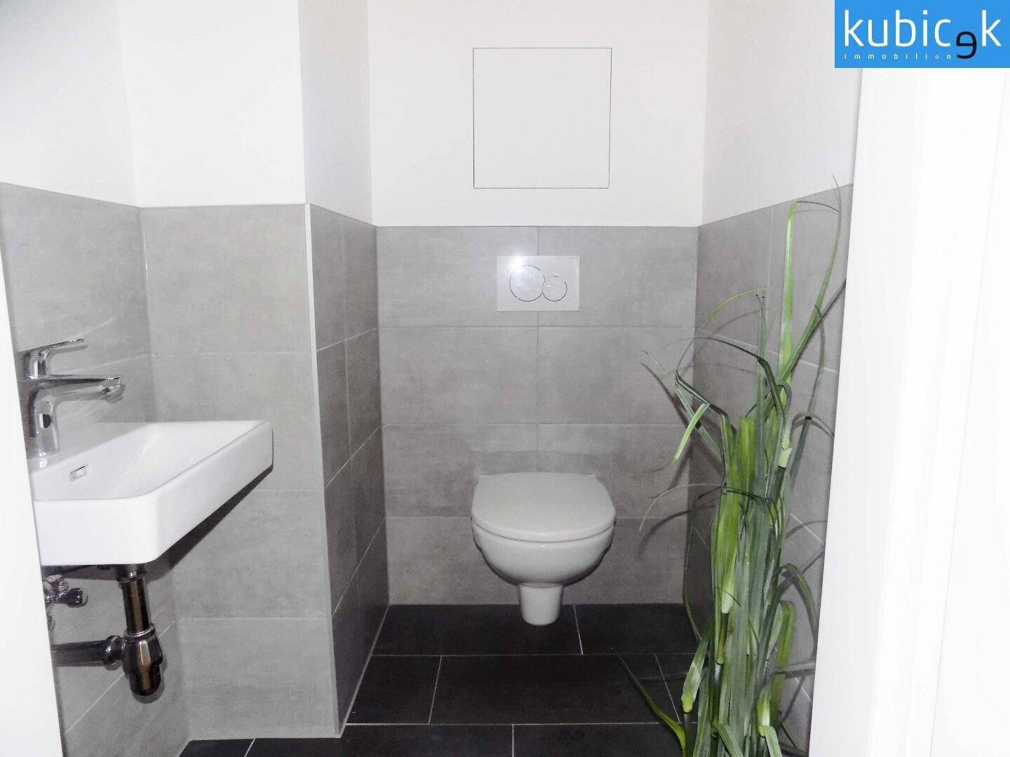 Modernes Gäste-WC mit Wand-WC, Einzelwaschbecken und grauen Wandfliesen.