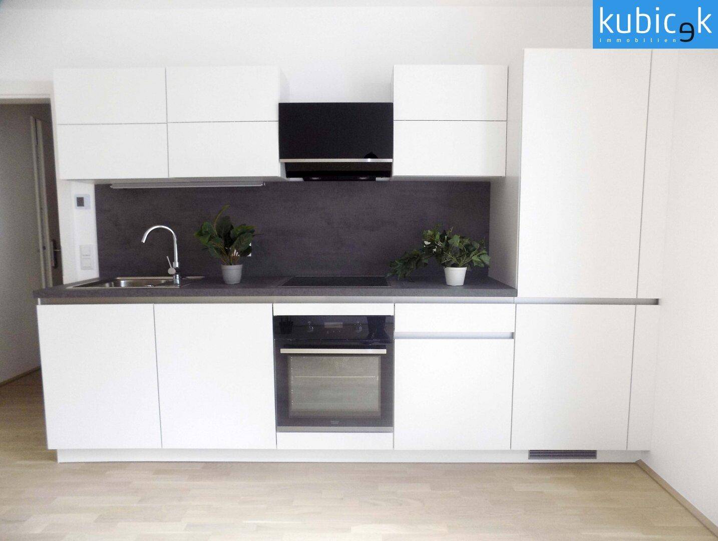 Moderne Einbauküche mit weißen Schränken, dunkler Arbeitsplatte und integriertem Backofen.