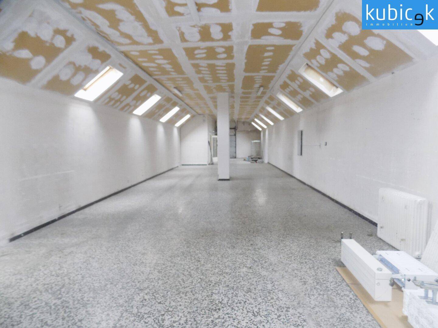 Langer, schmaler Raum mit schräger Decke, mehreren Dachfenstern und einem gesprenkelten Bodenbelag.