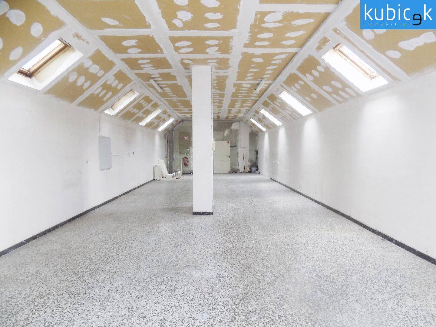 Geräumiger Lagerraum mit schräger Decke, Dachfenstern und einem robusten, gesprenkelten Bodenbelag.