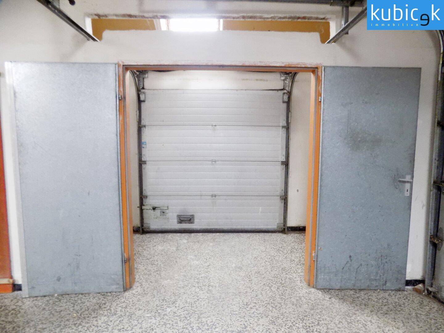 Innenansicht einer Garage oder Ladezone mit großem Rolltor und robustem, gesprenkeltem Bodenbelag.