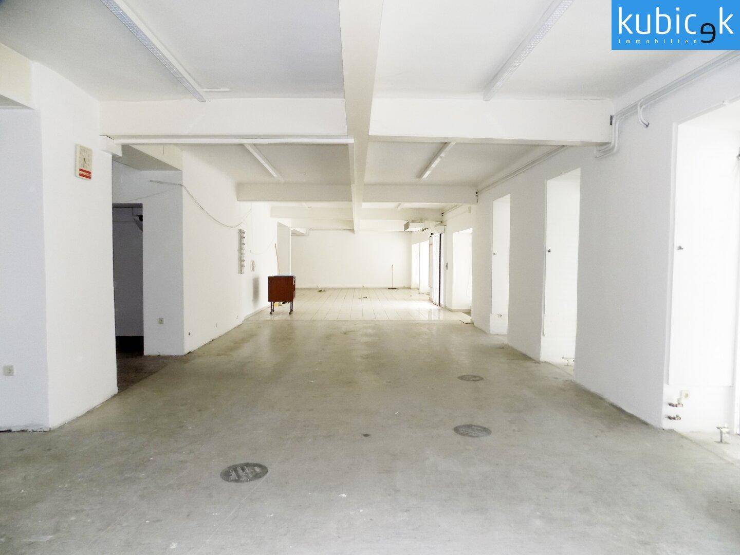 Großer, leerer Gewerberaum mit Betonboden, weißen Wänden und sichtbaren Deckenbalken, bereit zur Nutzung.