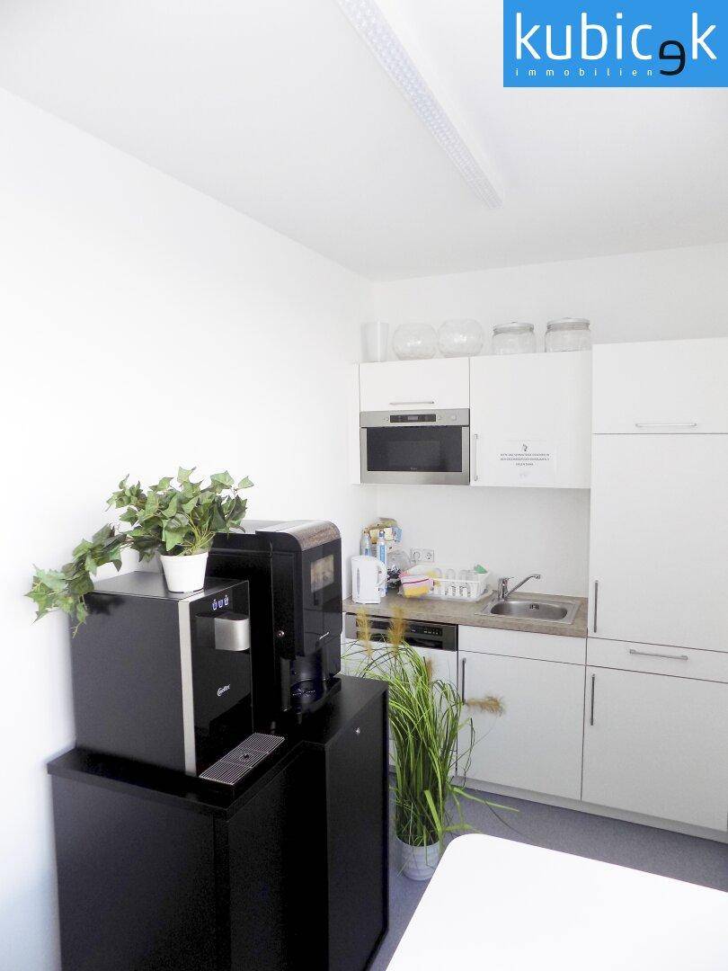 Kleine Küchenzeile mit weißen Schränken, Spüle, integrierter Mikrowelle und einer Kaffeemaschine.