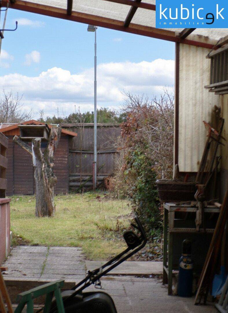 Überdachter Außenbereich im Garten mit Geräten und Blick ins Grüne.