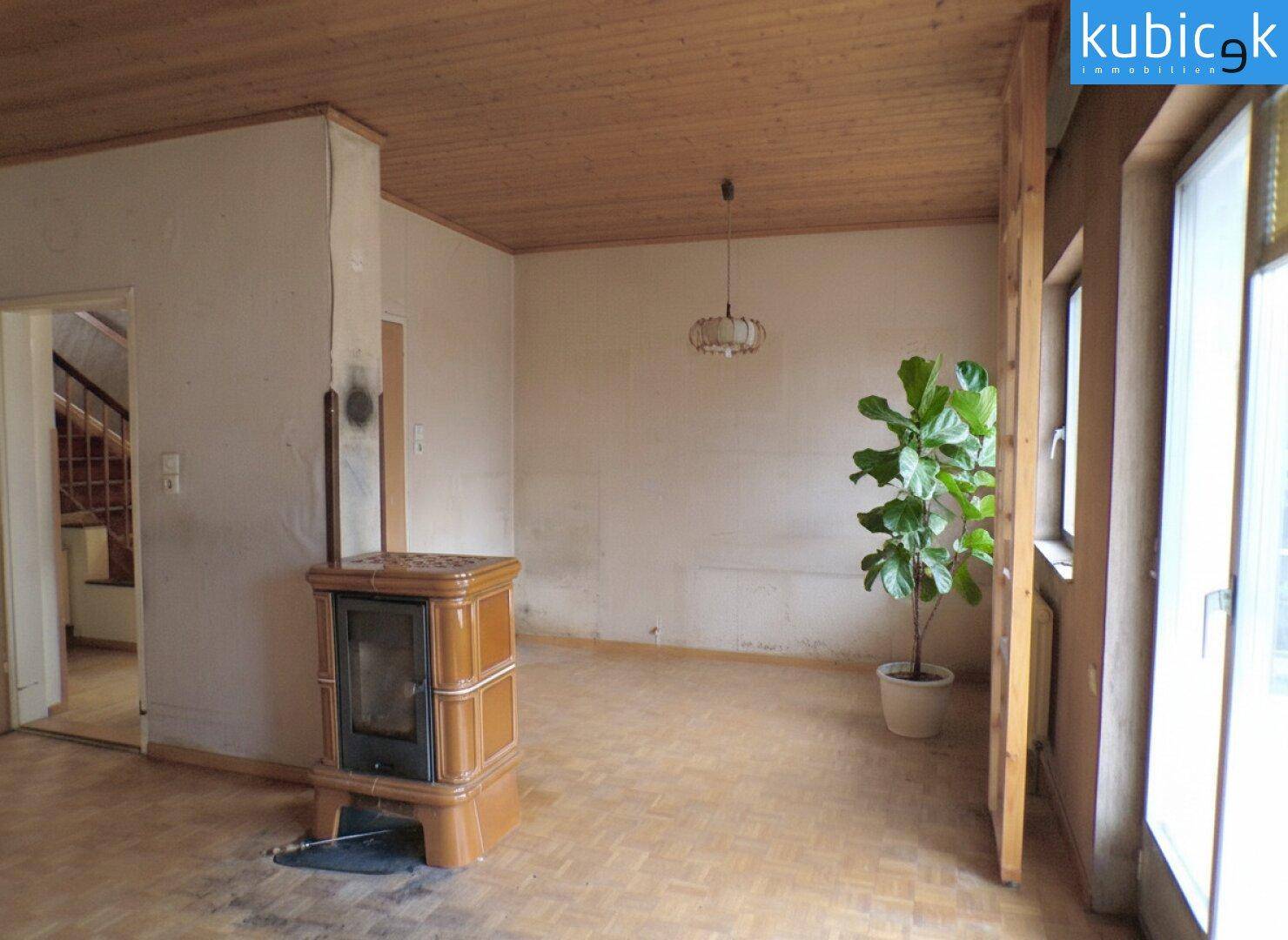 Geräumiges Wohnzimmer mit Holzdecke, Parkettboden und einem Kaminofen.