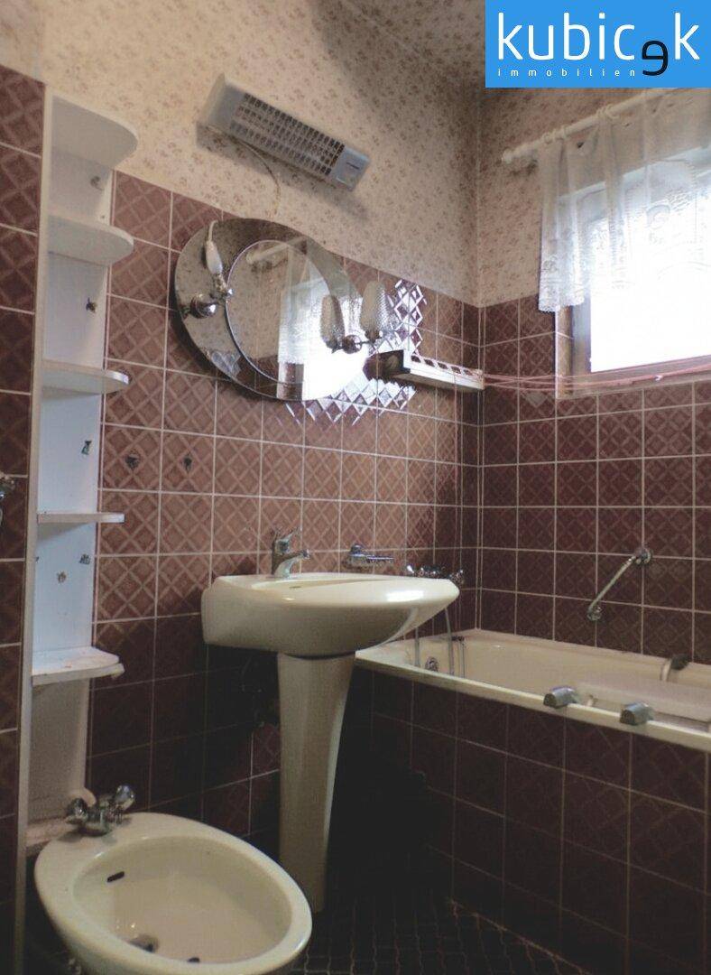 Badezimmer mit Badewanne, Waschbecken, Bidet und braunen Fliesen im 80er-Jahre-Stil.