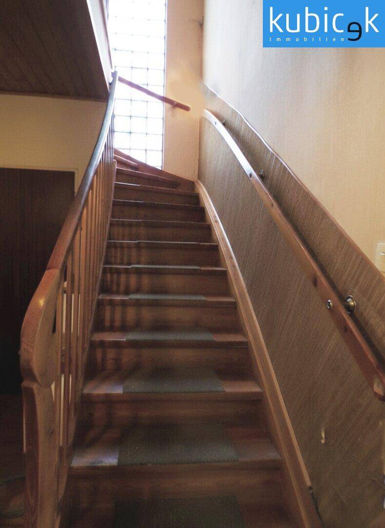 Holztreppe mit Geländer und einem hohen Fenster mit Glasbausteinen.