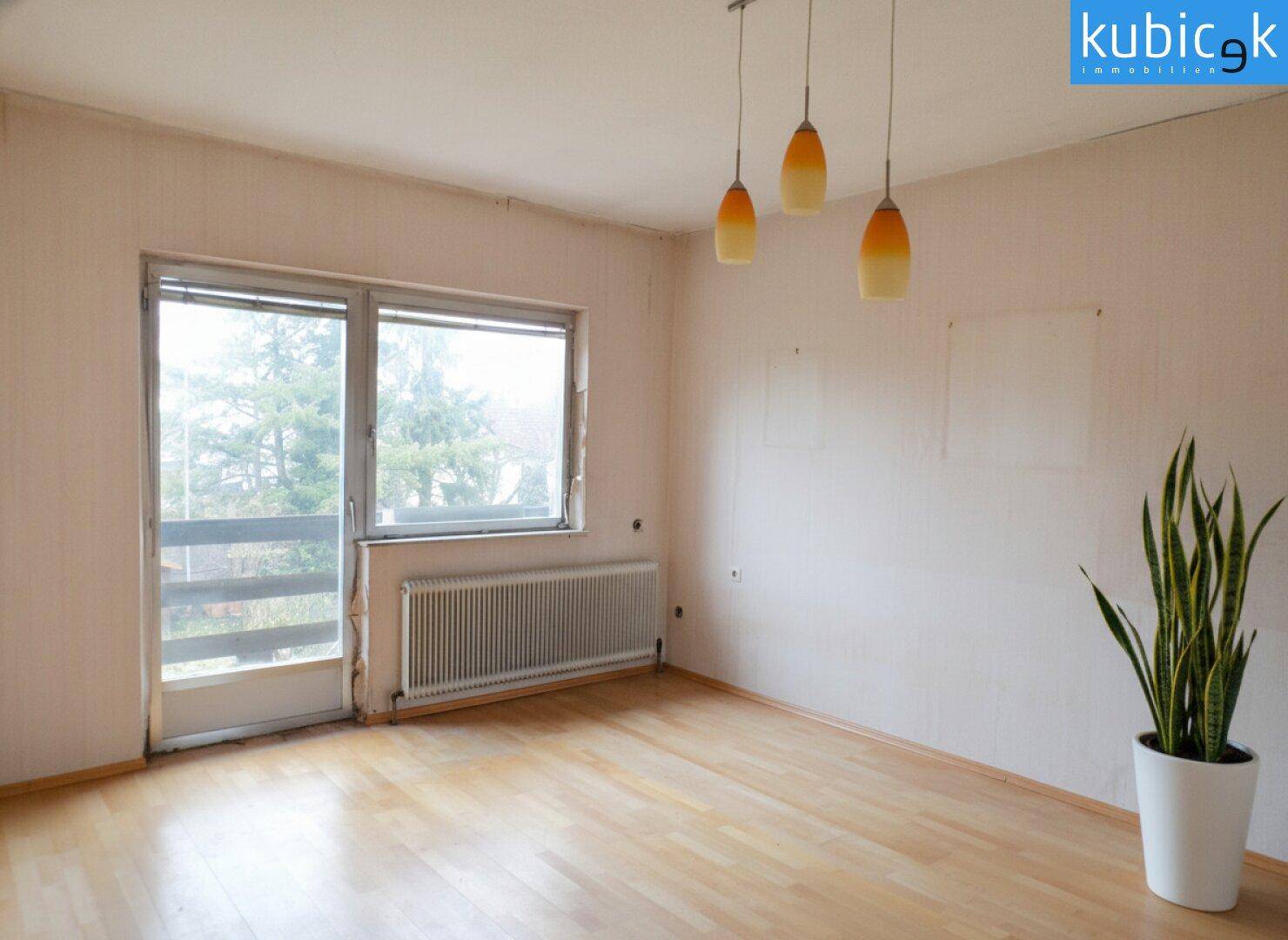 Helles Wohnzimmer mit Parkettboden, großem Fenster und Zugang zum Balkon.