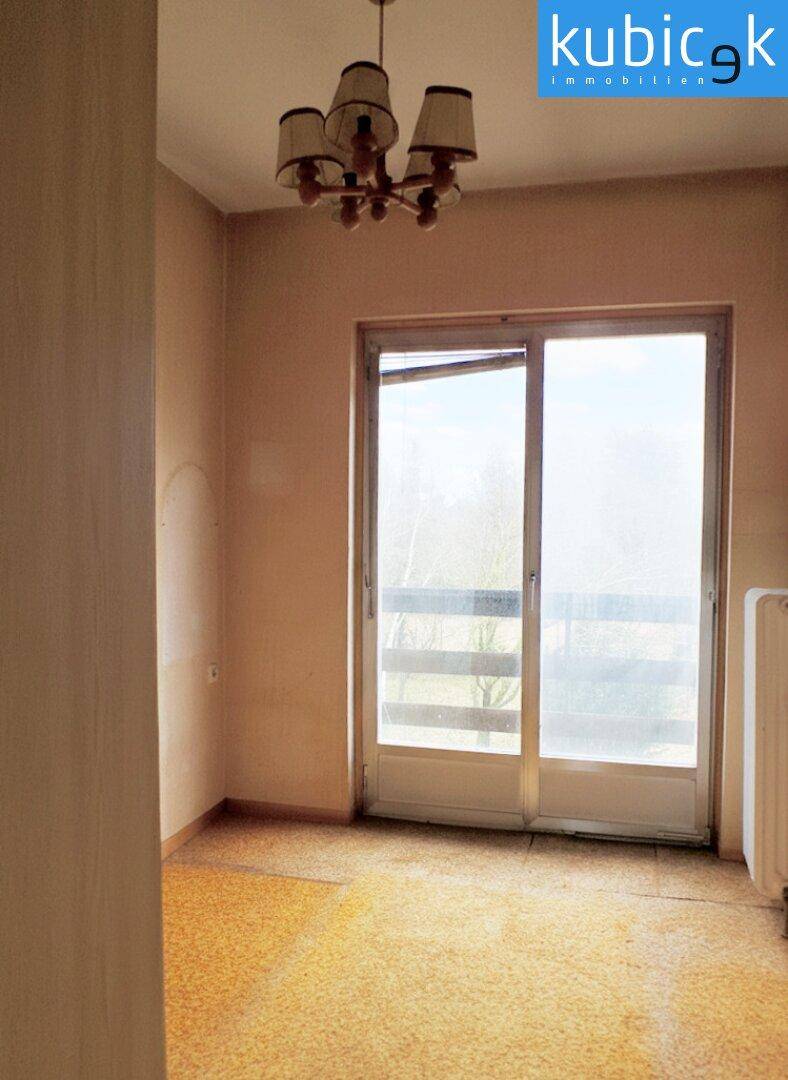 Raum mit Teppichboden und Balkonzugang, renovierungsbedürftig.