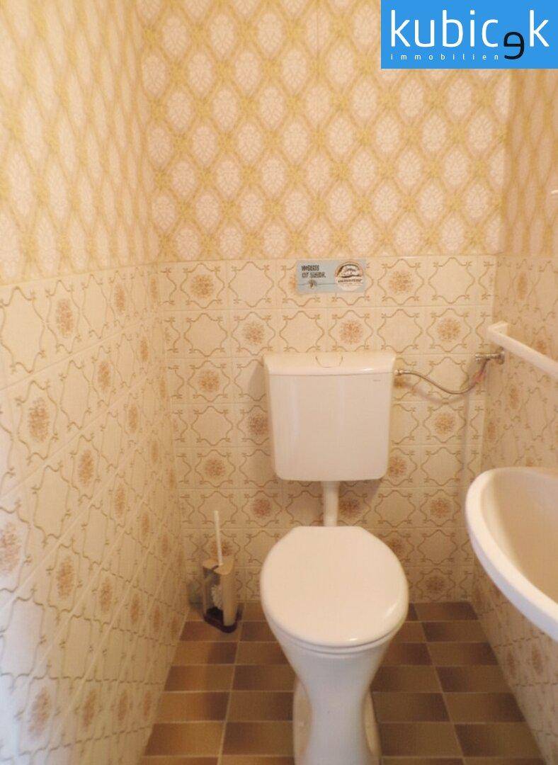 Separate Toilette mit WC, Waschbecken und gemusterten Fliesen.