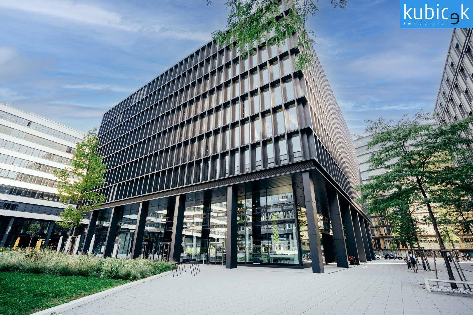 Weitläufige Ansicht eines modernen Bürogebäudes mit vielen Fenstern und umliegender Grünfläche.