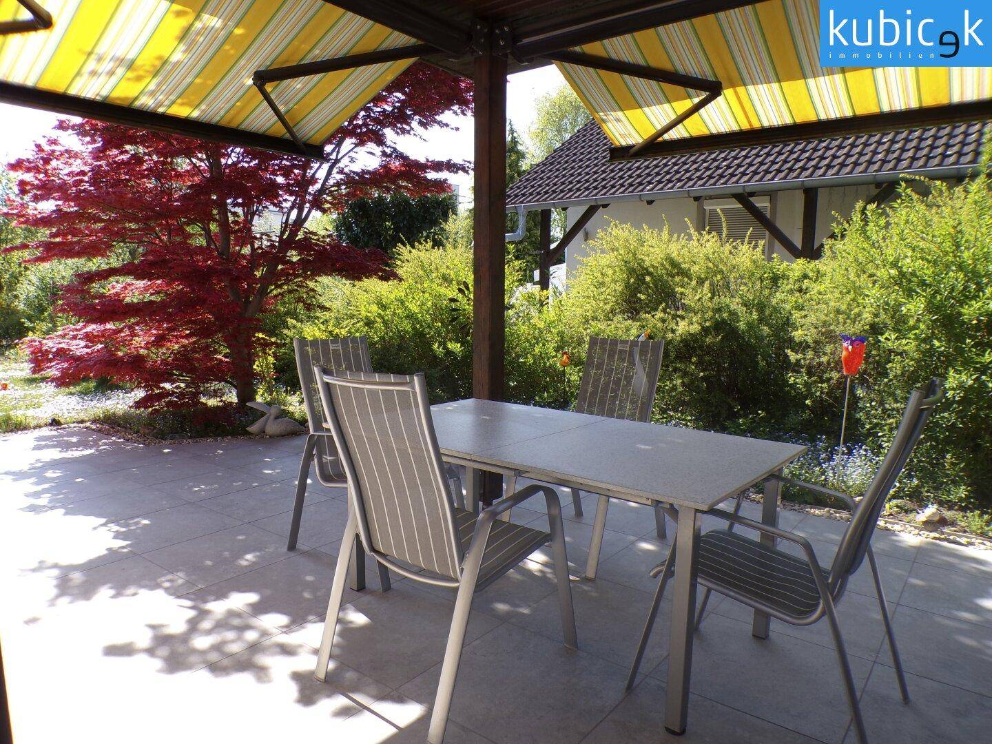 Möblierte Terrasse mit Esstisch und Stühlen unter einer gestreiften Markise.