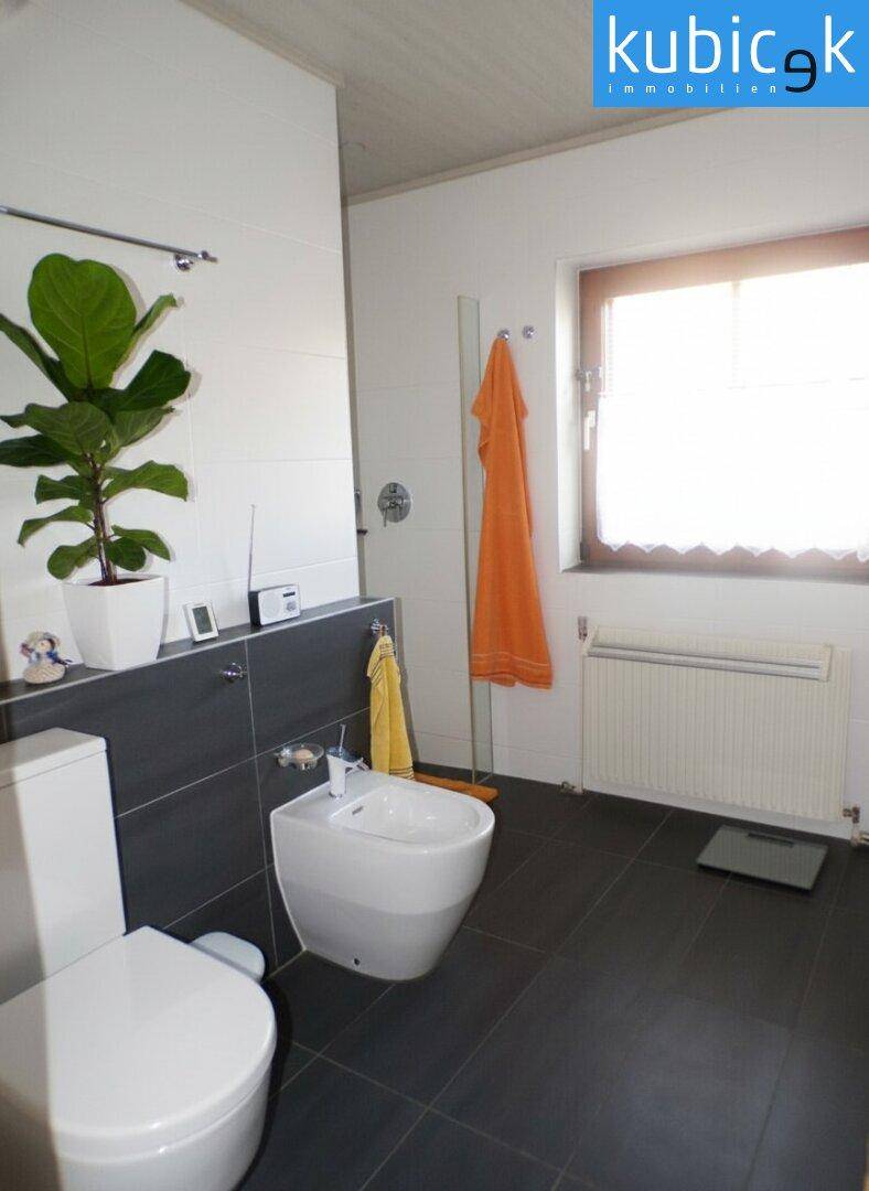 Modernes Badezimmer mit dunklen Fliesen, Toilette, Bidet, Dusche und Fenster.