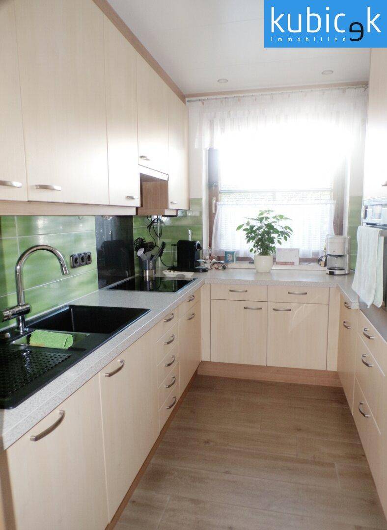 Helle Küche mit beigen Schränken, grünen Fliesen und Fenster für natürliches Licht.