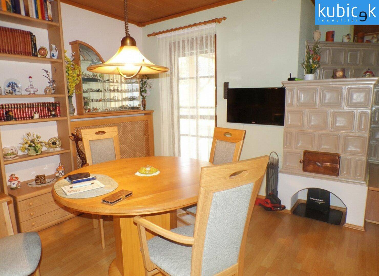 Gemütlicher Essbereich mit Holztisch, Stühlen und einem traditionellen Kachelofen.