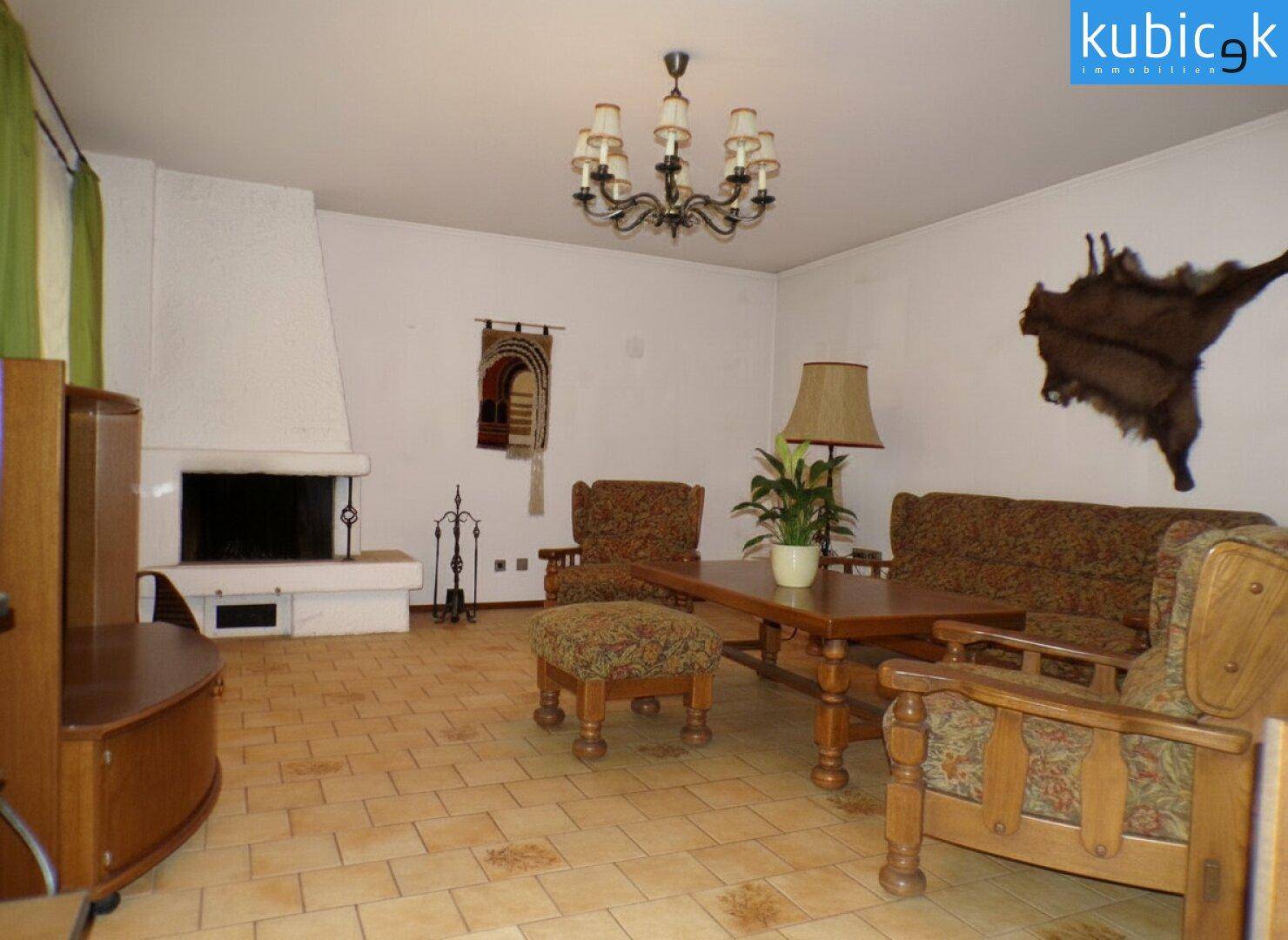 Geräumiges Wohnzimmer mit Kamin, traditionellen Möbeln und Fliesenboden.