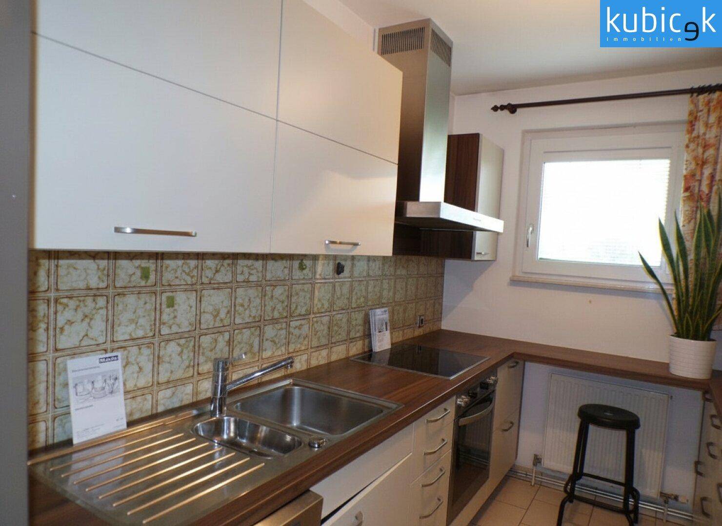 Helle Küche mit weißen Schränken, Edelstahlspüle und gemusterten Wandfliesen.