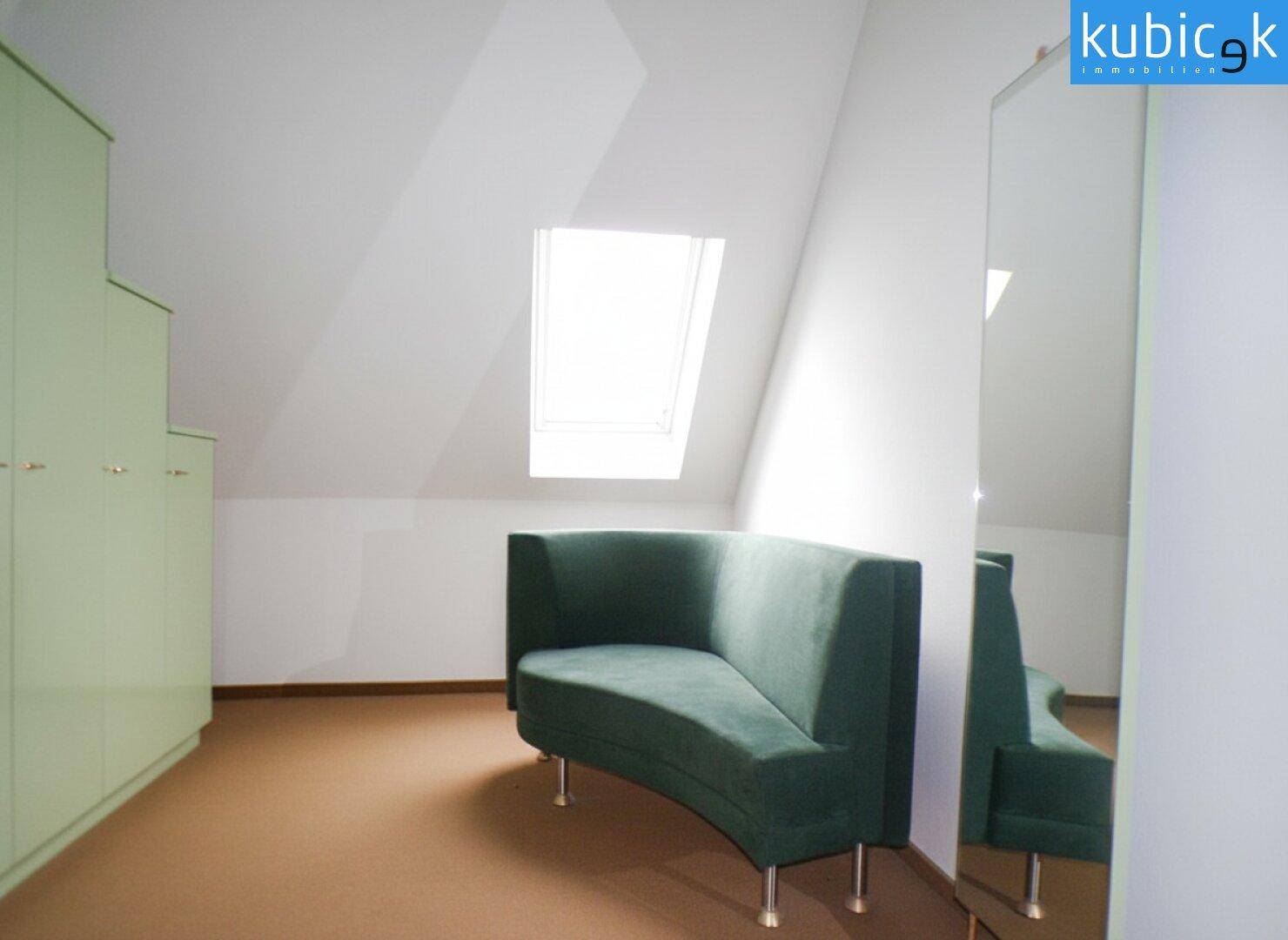 Dachzimmer mit grünem Sofa, Dachfenster und schrägen Wänden.