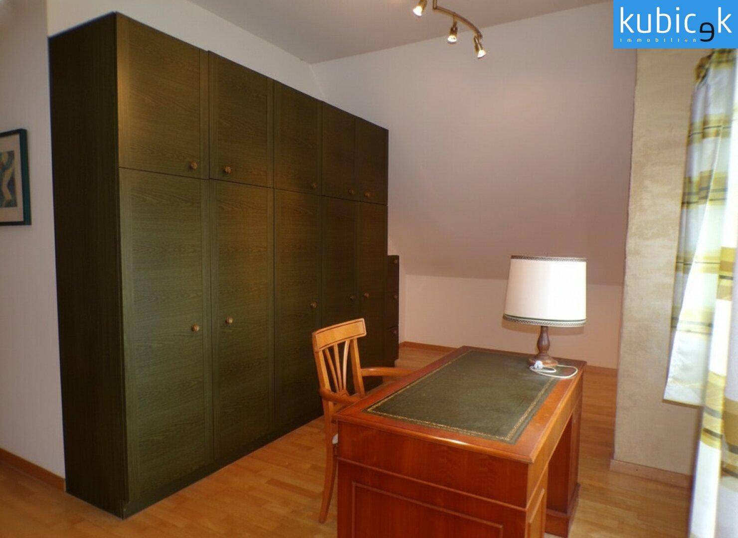 Dachgeschoss-Büro mit großem Schreibtisch und integrierten Kleiderschränken.
