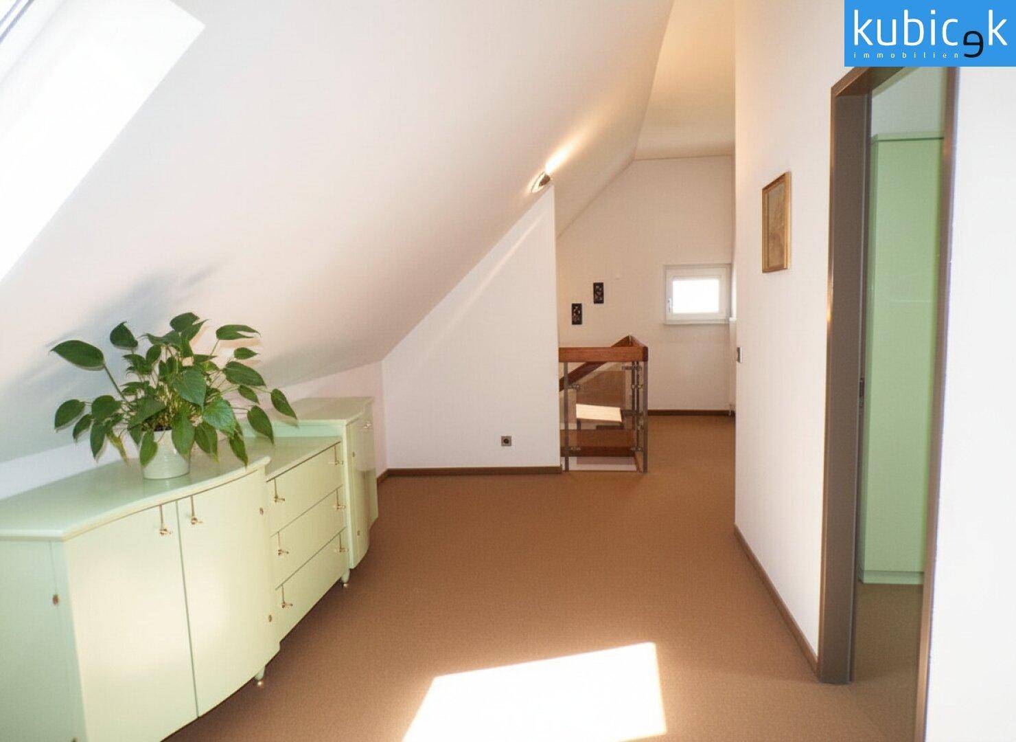 Heller Flur im Dachgeschoss mit schrägen Wänden und Kommode.