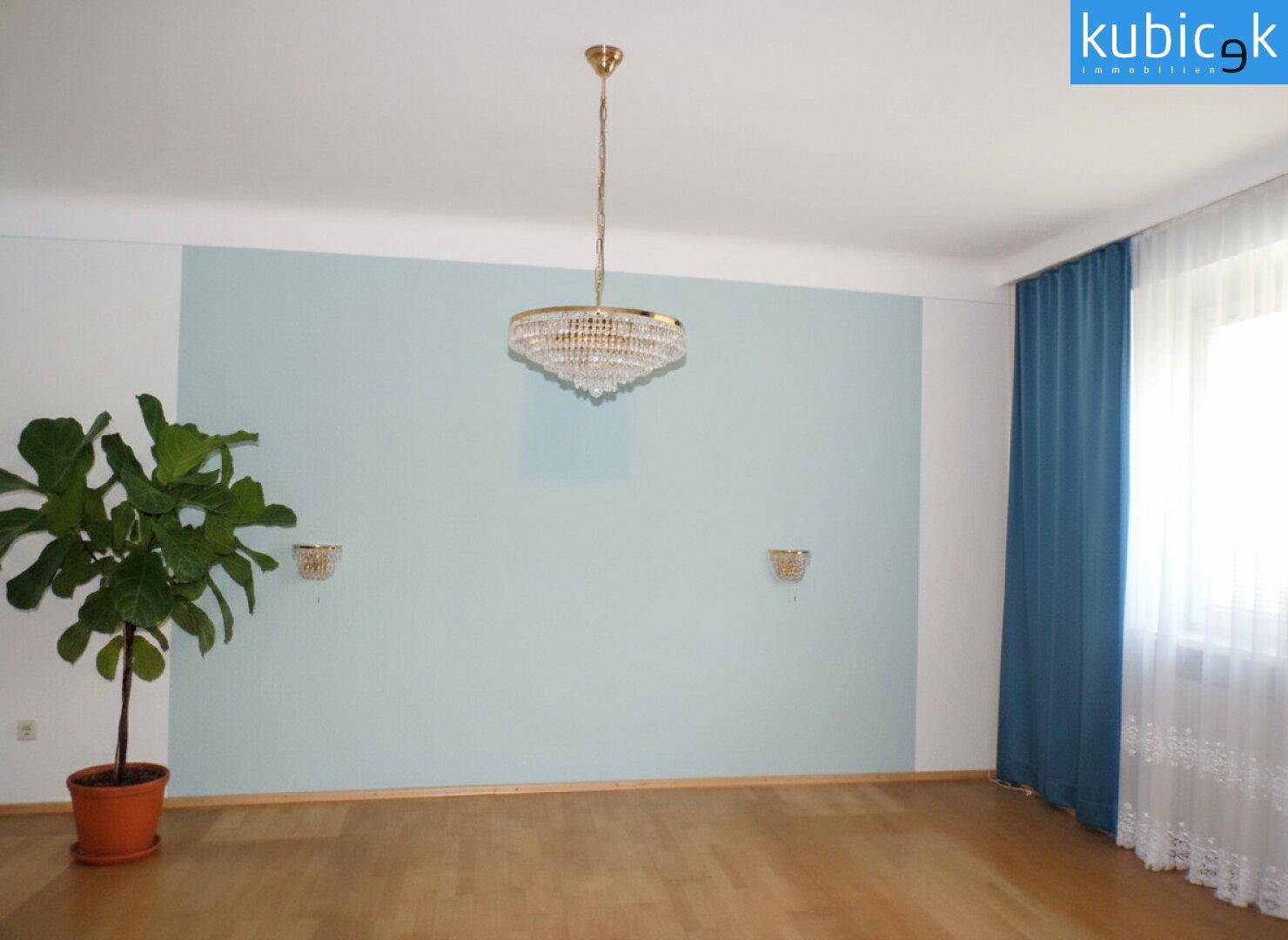 Helles Zimmer mit Parkettboden, einer hellblauen Akzentwand und einem Kronleuchter.
