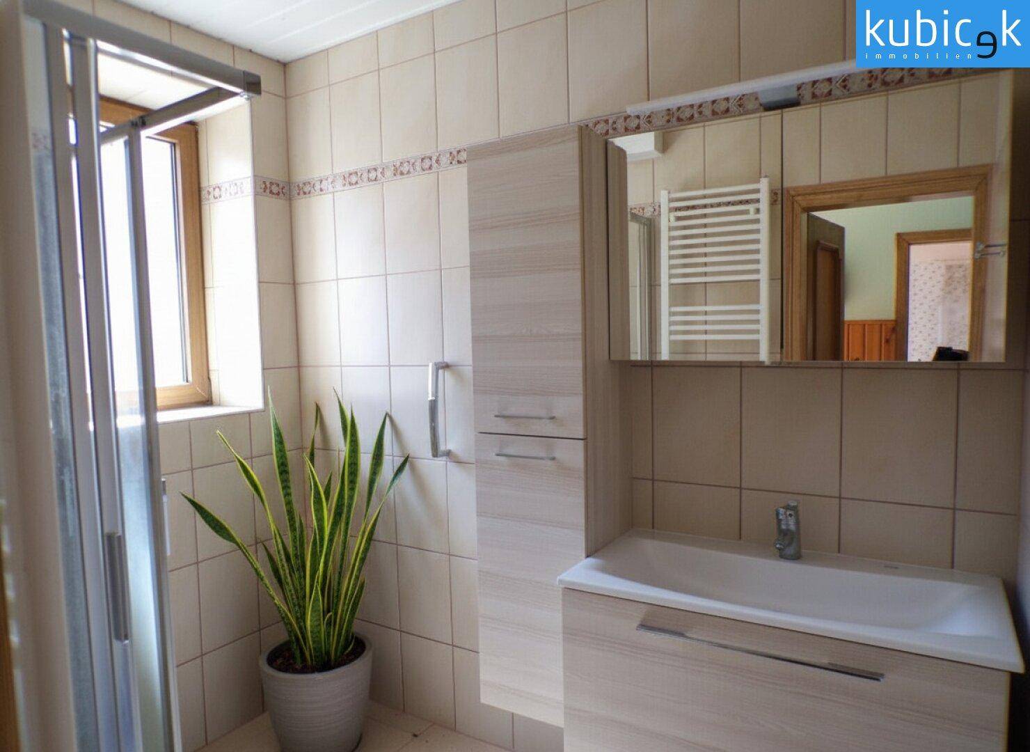 Modern gefliestes Badezimmer mit Duschkabine, Waschtisch und Spiegelschrank.
